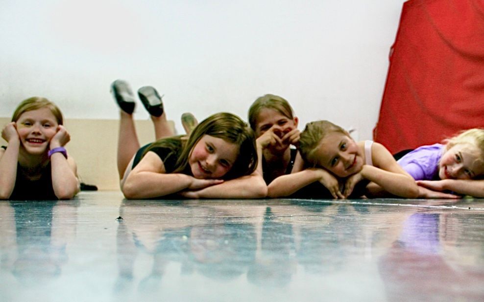 A group of young girls are laying on their stomachs on the floor.