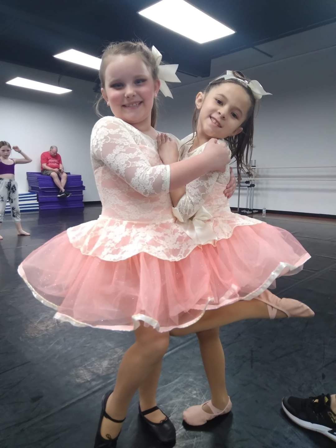 Two little girls are hugging each other in a dance studio