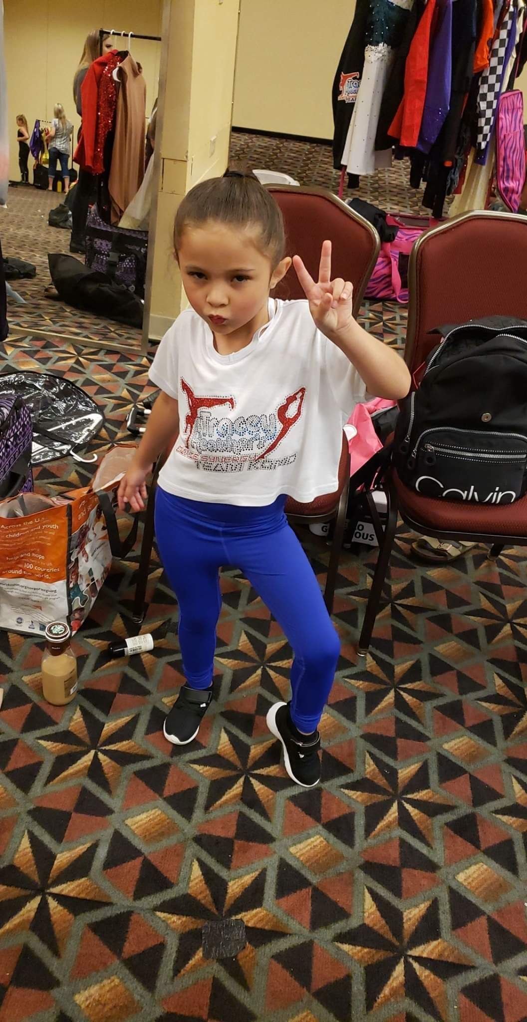 A little girl is standing in a room giving a peace sign.