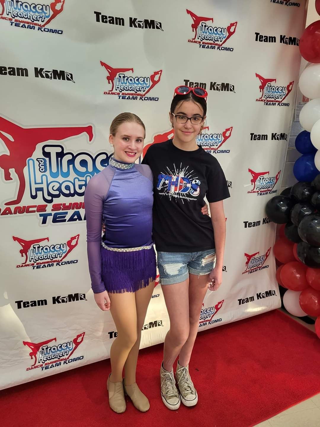 Two young girls are posing for a picture in front of a wall that says trac heat