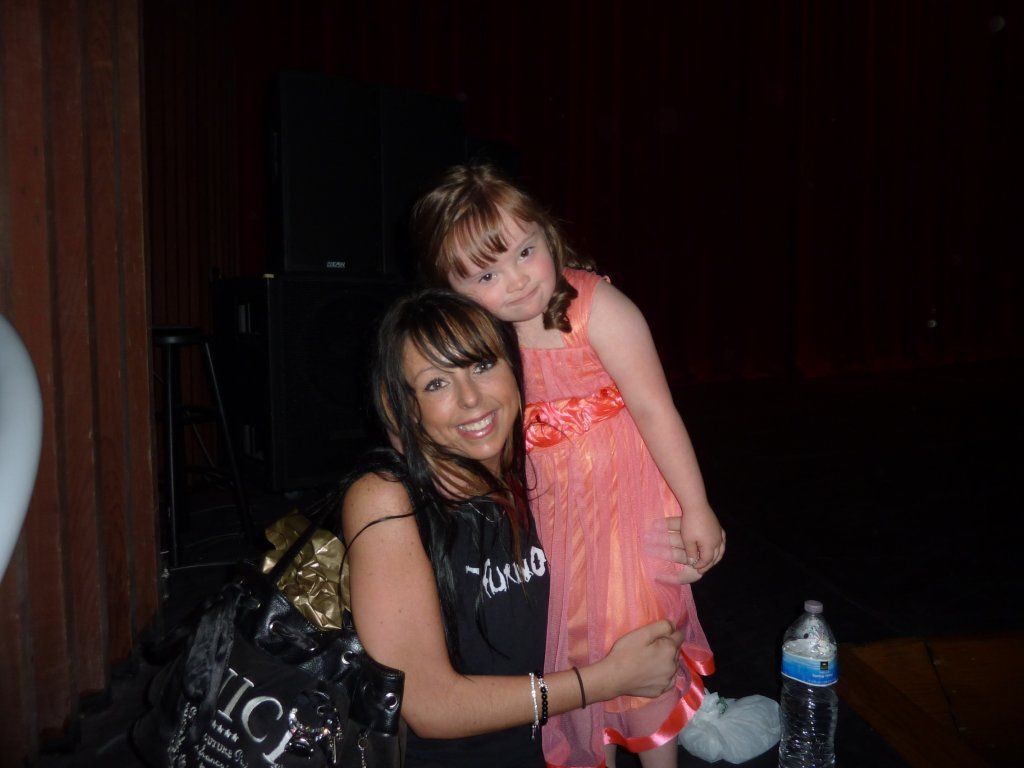 A woman is hugging a little girl who is wearing a pink dress