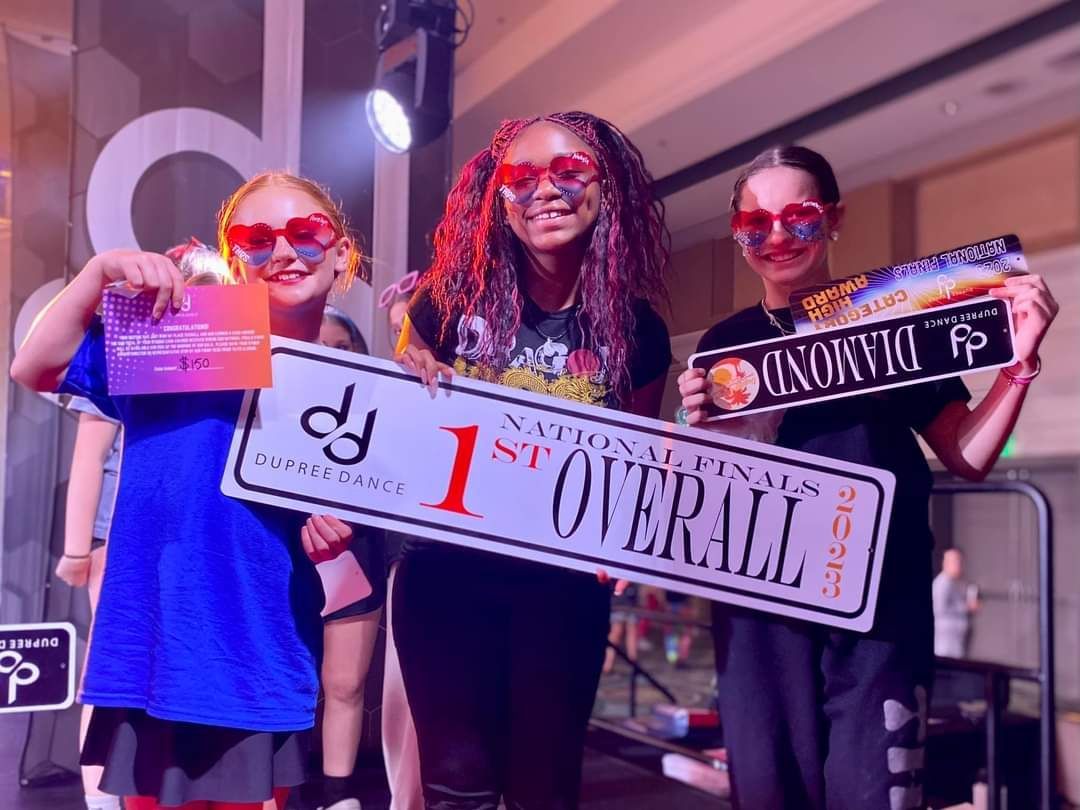 Three girls are holding up a sign that says 1st overall