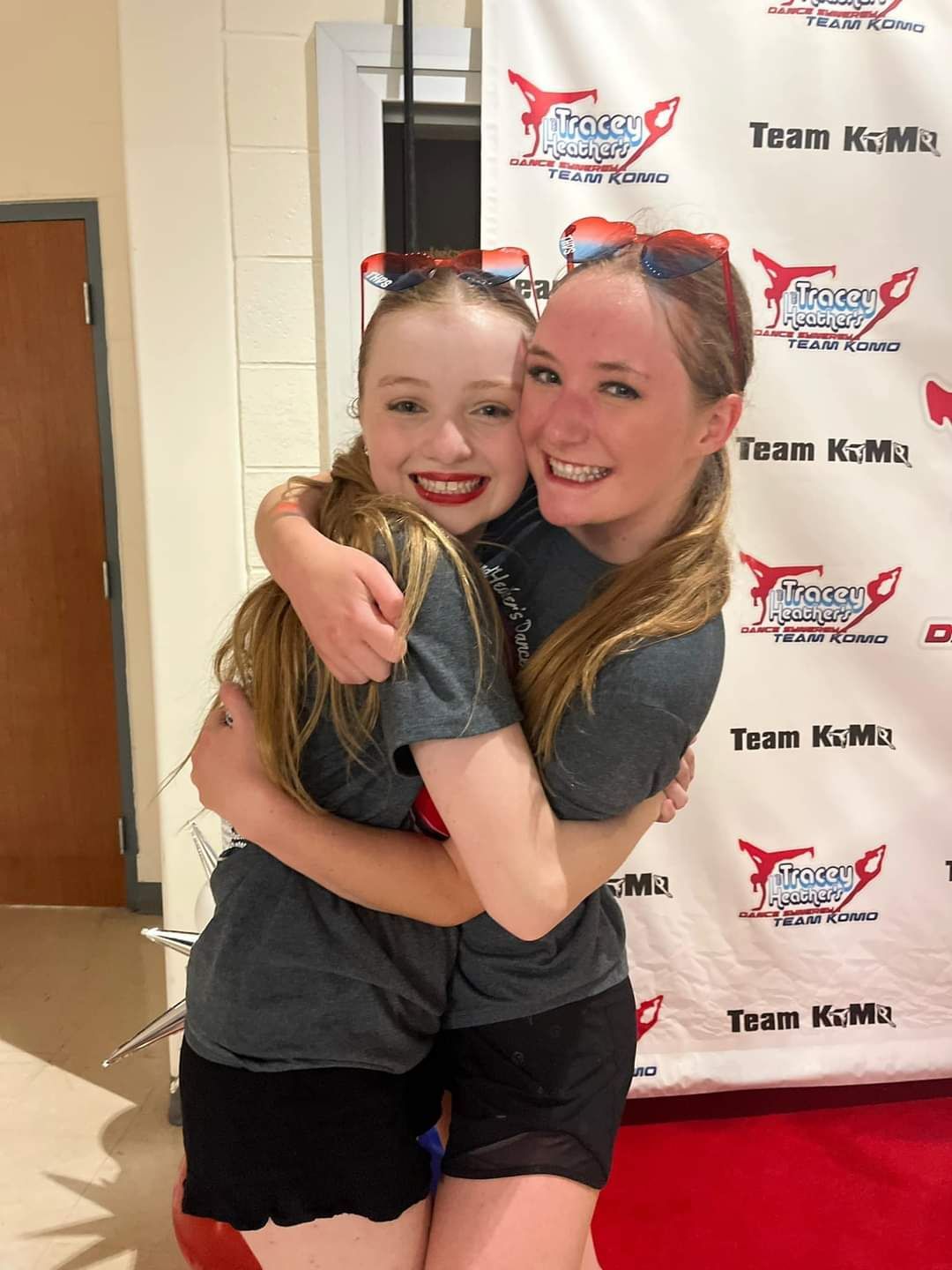 Two girls hugging in front of a team kmu banner