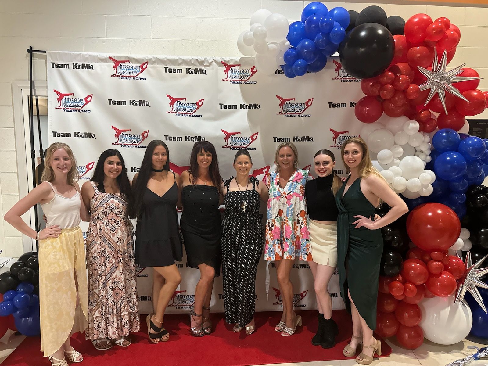 A group of women are posing for a picture in front of a wall of balloons.