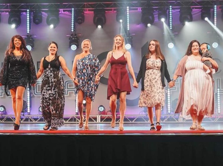 A group of women are standing on a stage holding hands.