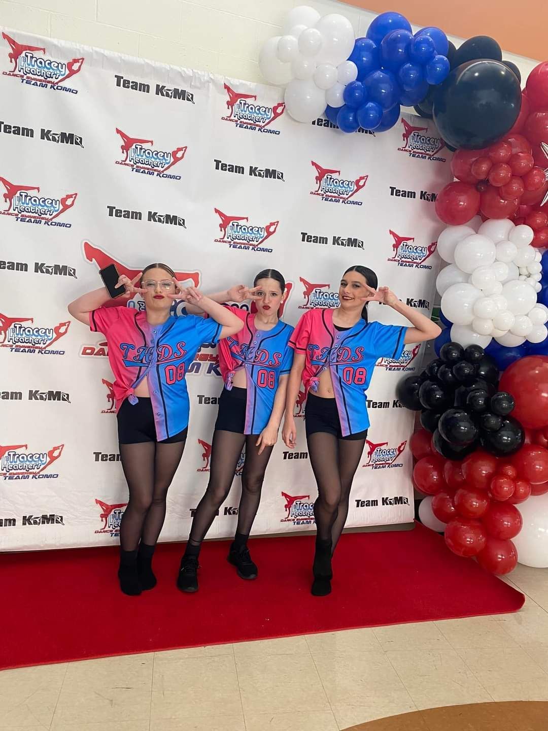 Three women are standing in front of a wall covered in balloons.