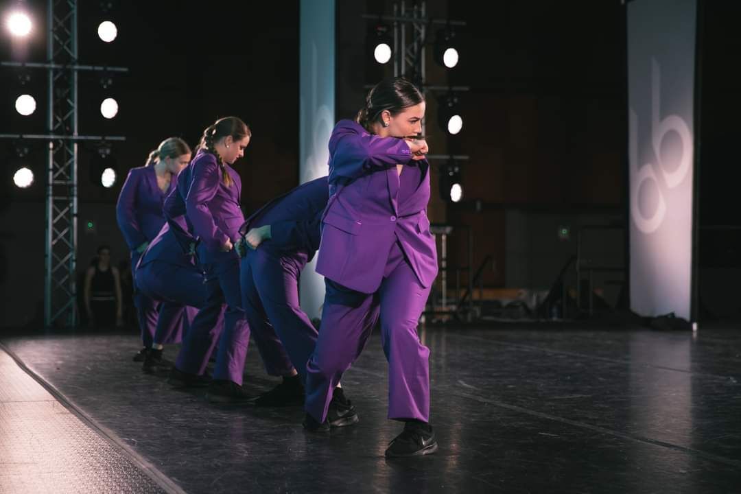 A group of people in purple suits are dancing on a stage.
