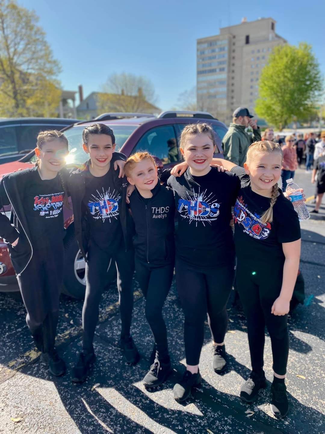 A group of young girls are posing for a picture in a parking lot.
