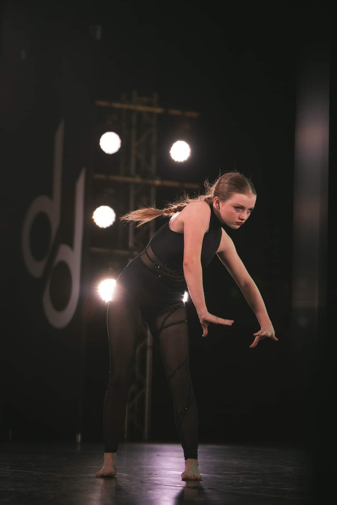 A young woman is dancing on a stage in a dark room.