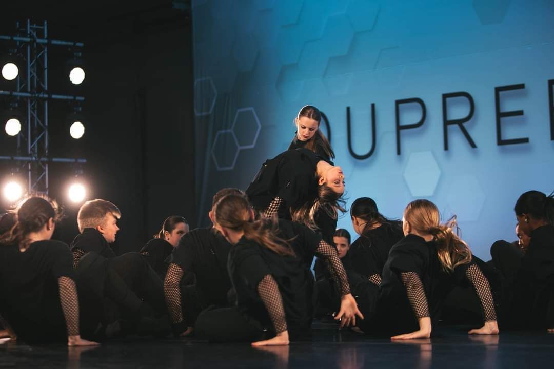 A group of people are dancing on a stage in front of a sign that says upre.