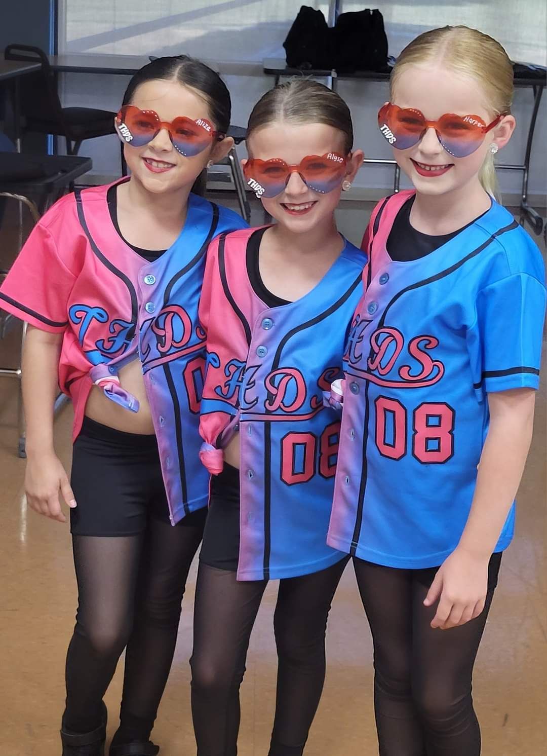 Three girls wearing baseball jerseys with the number 08 on them