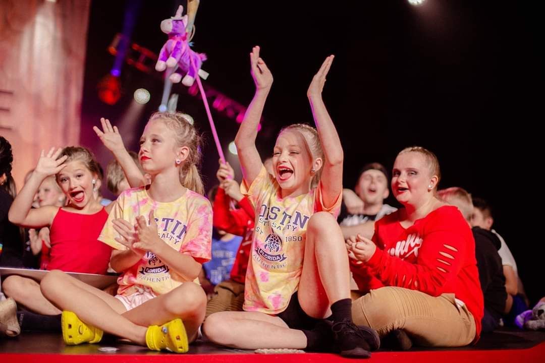 A group of young girls are sitting on the floor with their arms in the air.