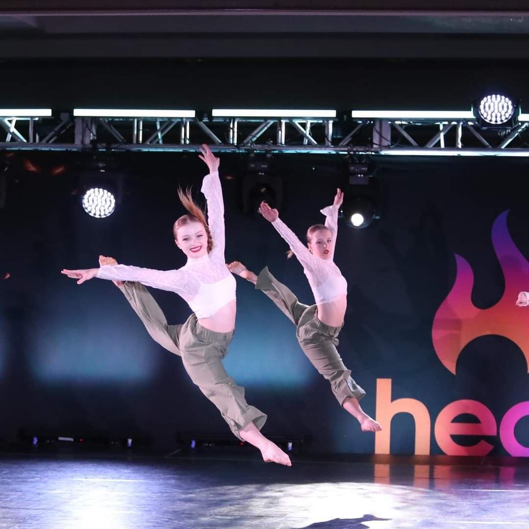Two young girls are dancing in front of a sign that says heat