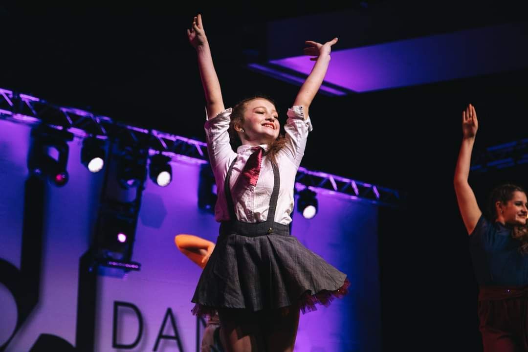 A girl is dancing on a stage with her arms in the air.