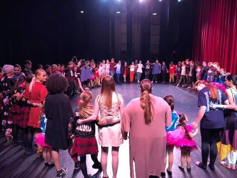 A group of people are standing on a stage holding hands.