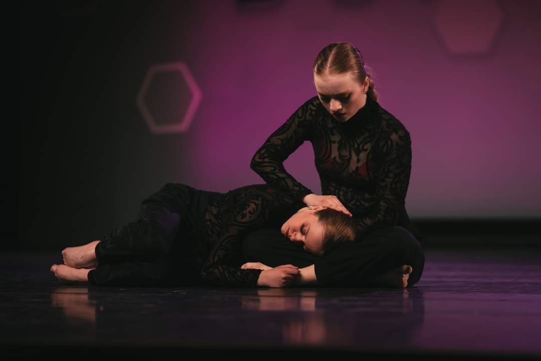 Two women are dancing on a stage and one is laying on the floor.