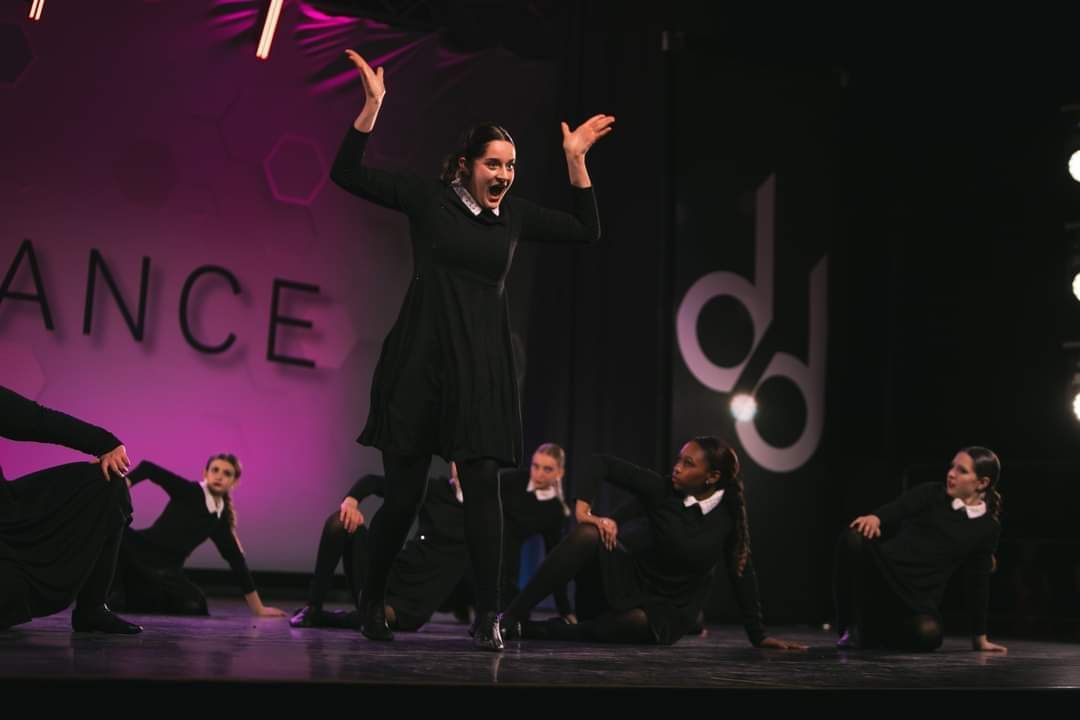 A group of people are dancing on a stage in front of a sign that says dance