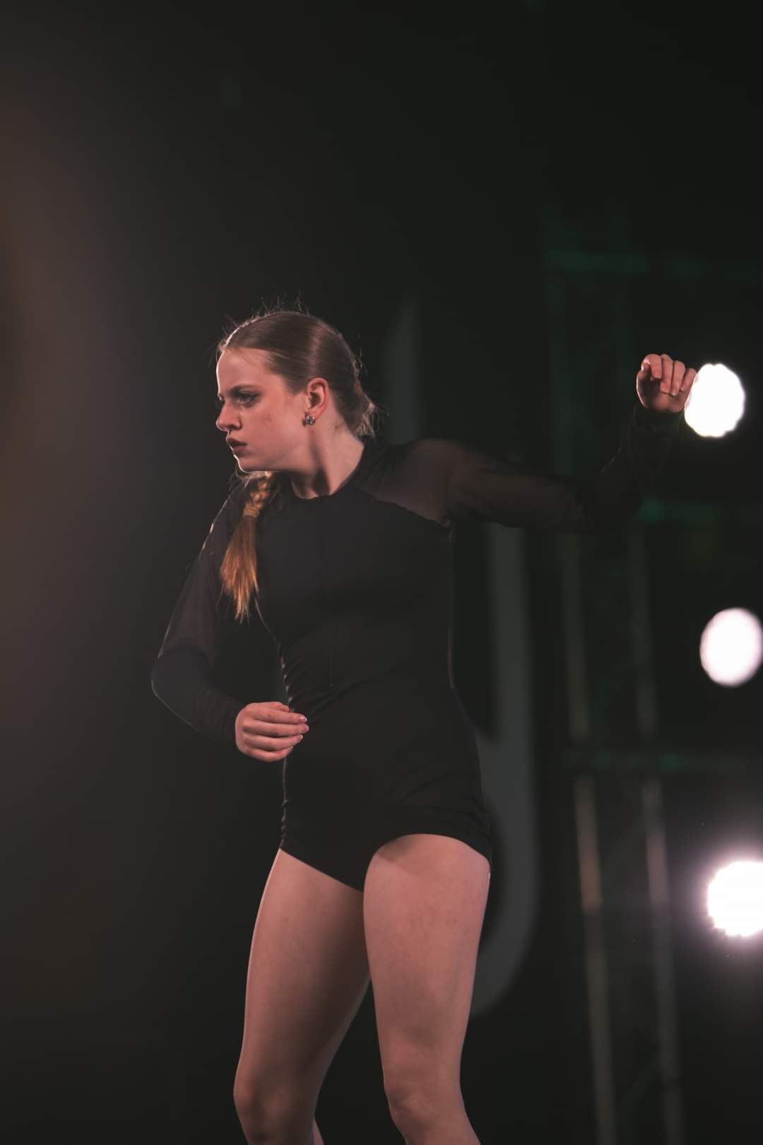A woman in a black leotard is dancing on a stage.