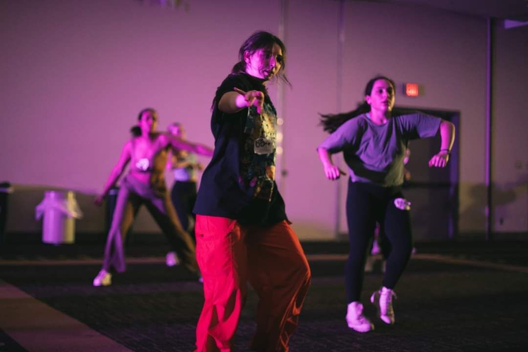 A group of young women are dancing in a room with purple lights.