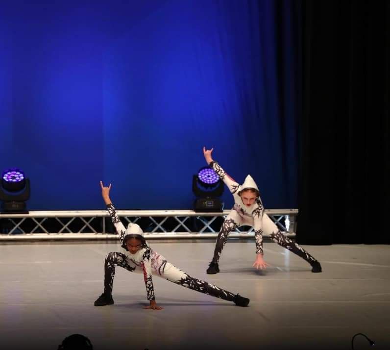 Two dancers perform on a stage in front of a blue curtain