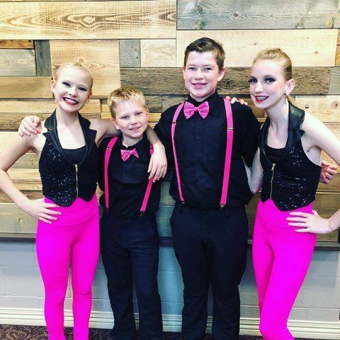 A group of young dancers are posing for a picture in front of a wooden wall.