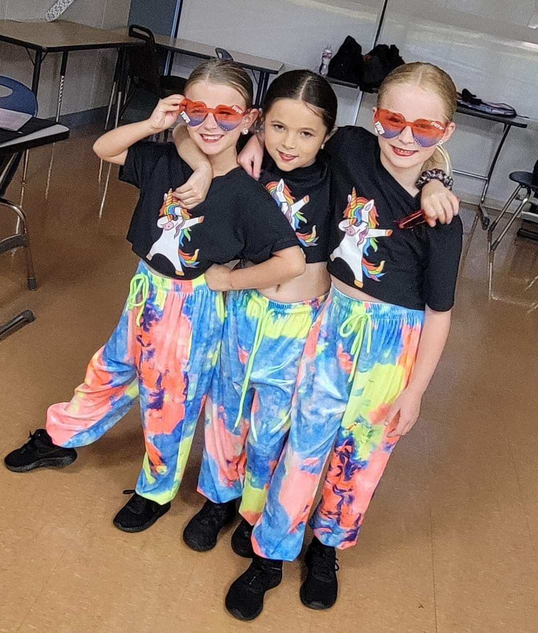 Three young girls wearing colorful outfits and sunglasses are posing for a picture.