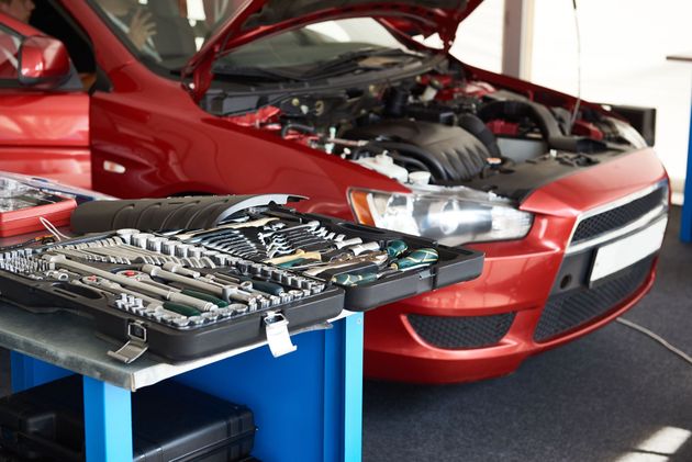 Red sports car with hood open beside a tool cart in a garage or workshop