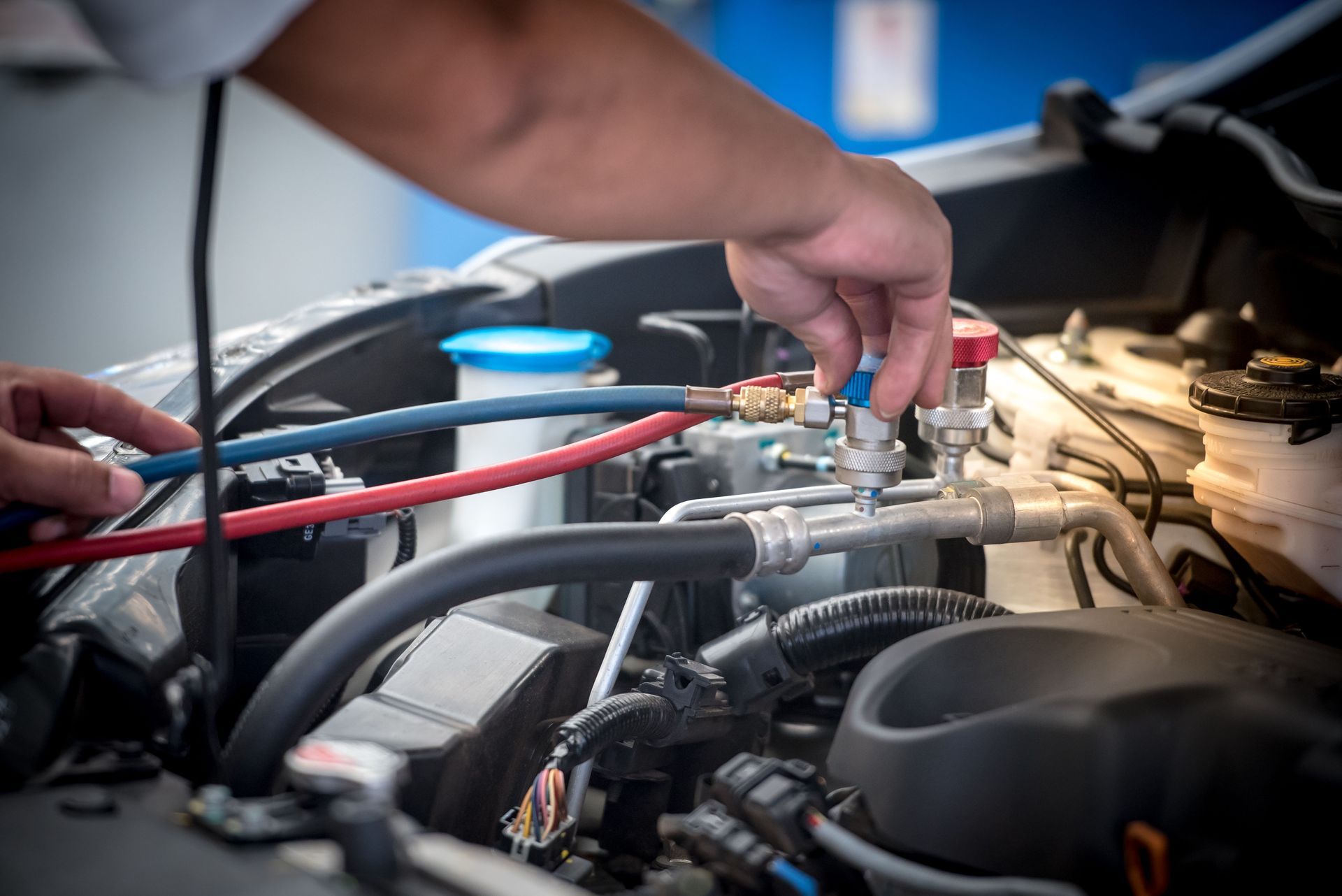 Mechanic adjusting engine components in a car bay, with hoses and tools visible