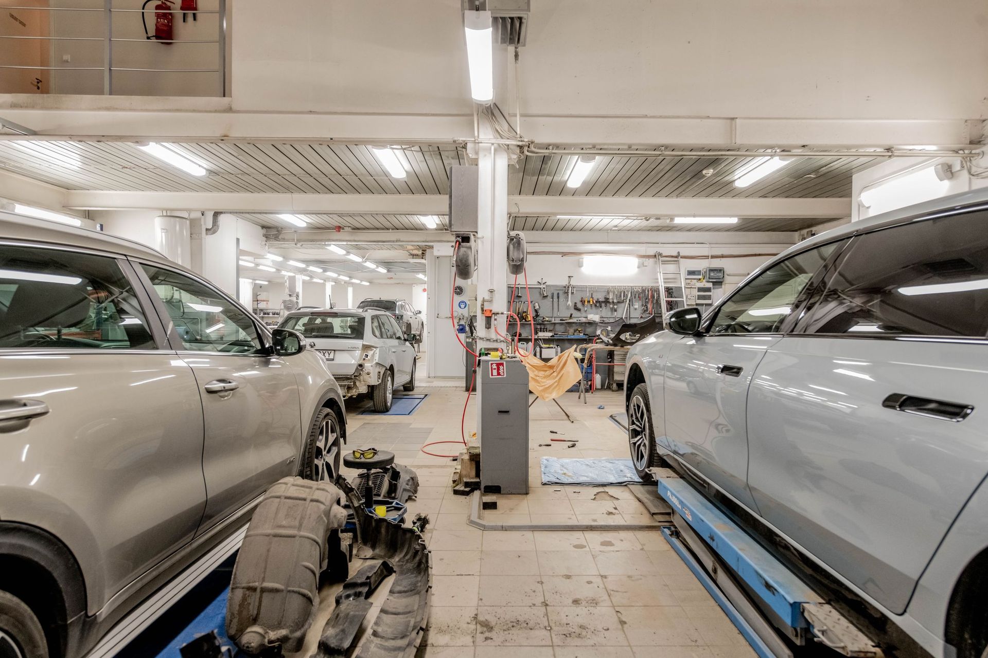 Automotive factory interior with two silver cars on assembly equipment and tools in the center aisle