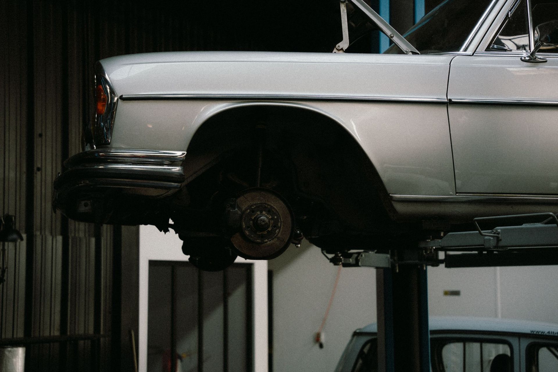 Silver classic car on a lift in a garage, showing the front wheel removed and exposed brake hub.
