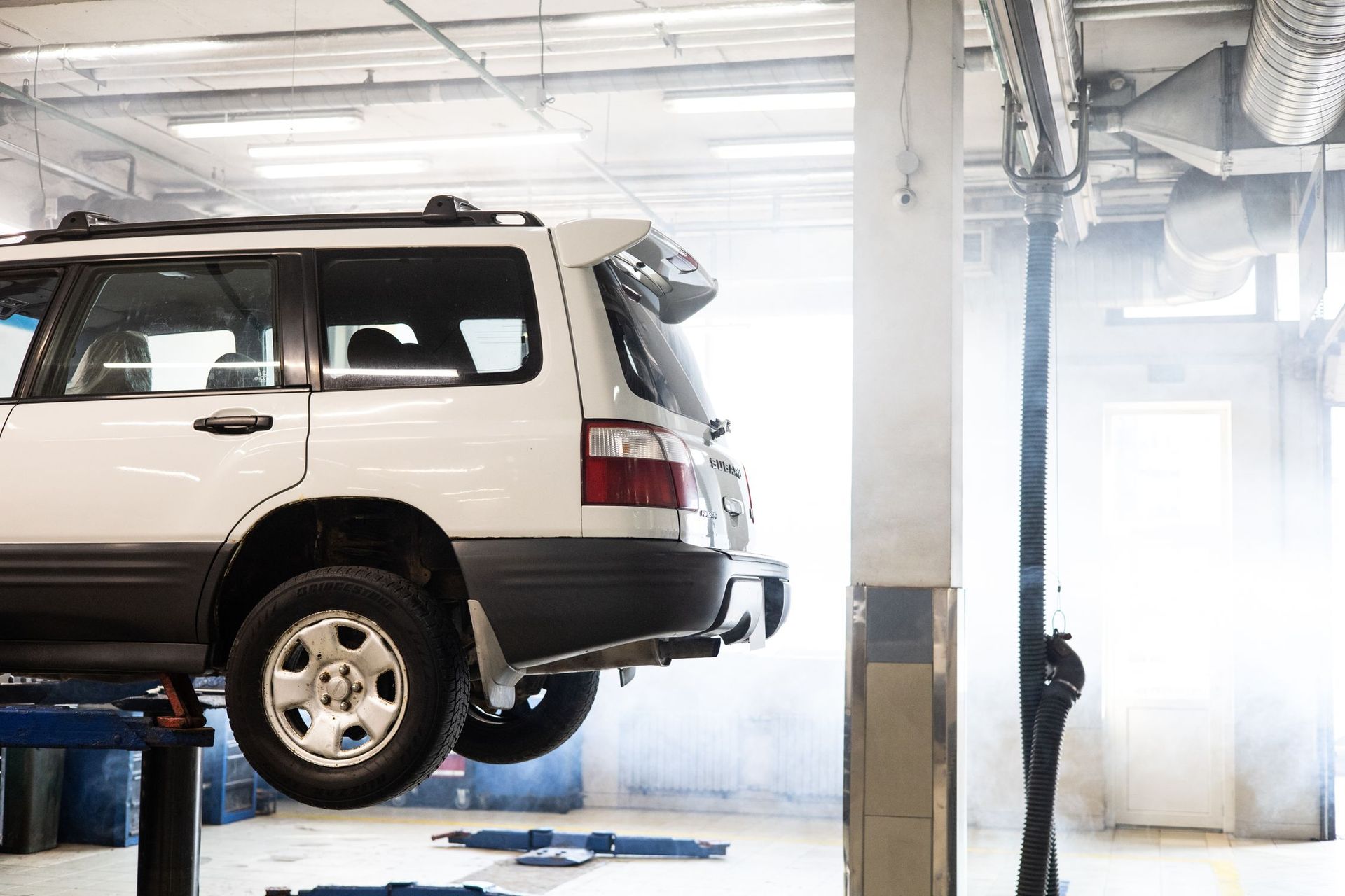 White SUV on a lift in an auto repair garage with bright light and tools nearby