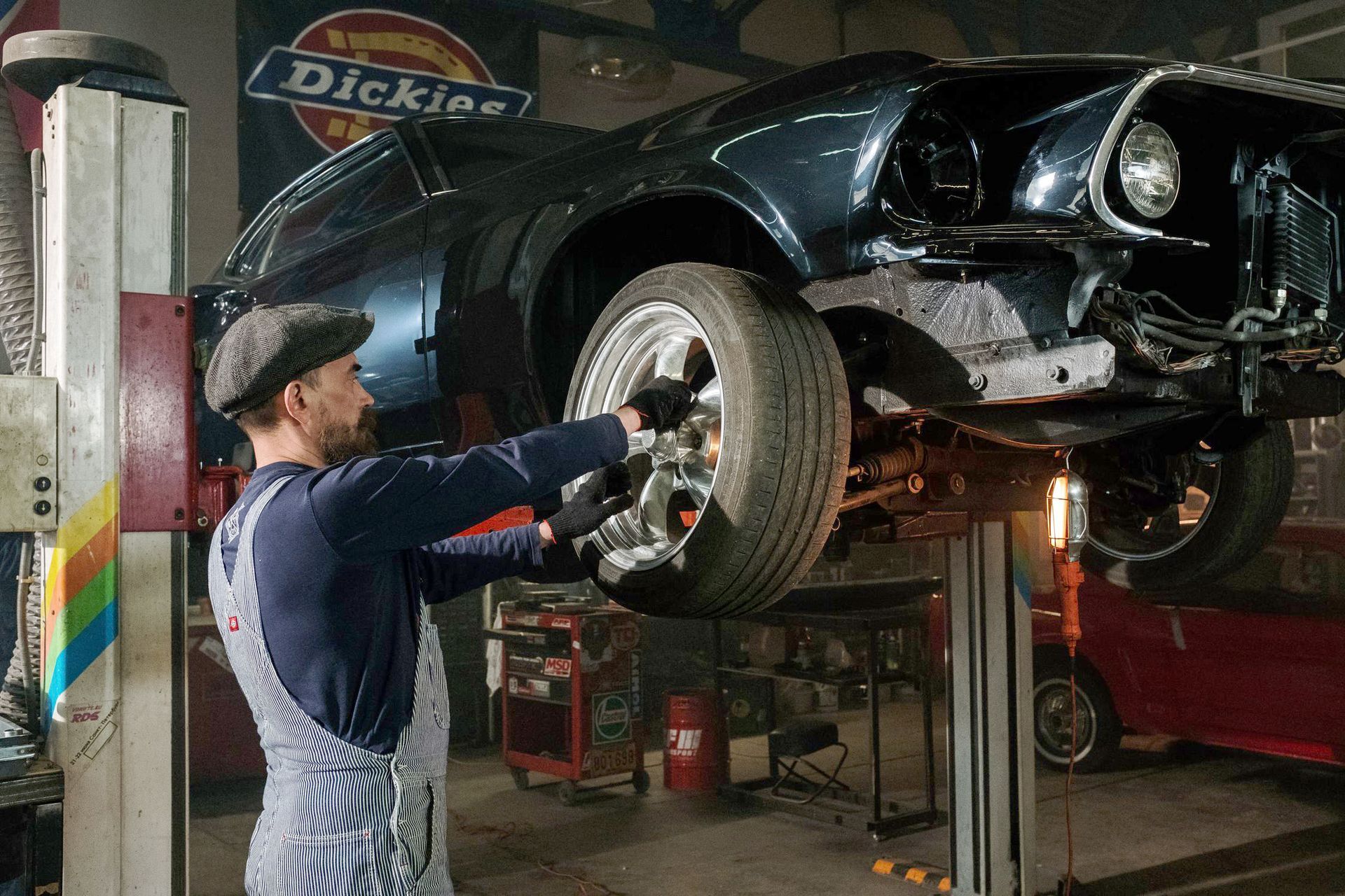 Mechanic in blue coveralls working under a raised car in an auto repair shop