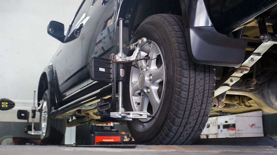 Black truck undergoing wheel alignment; diagnostic equipment attached to tires.