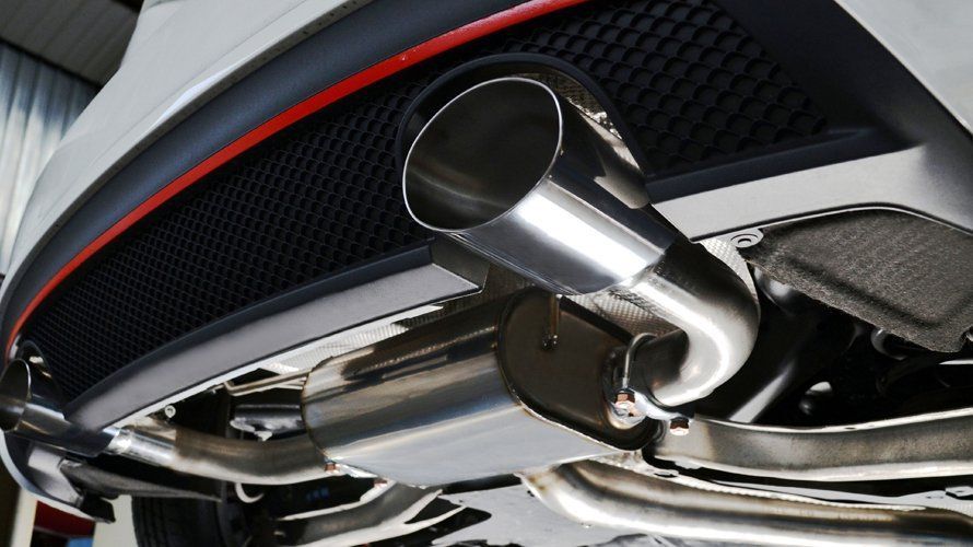 Close-up of a car's exhaust system, with a polished metal tailpipe against a black grille and red trim.