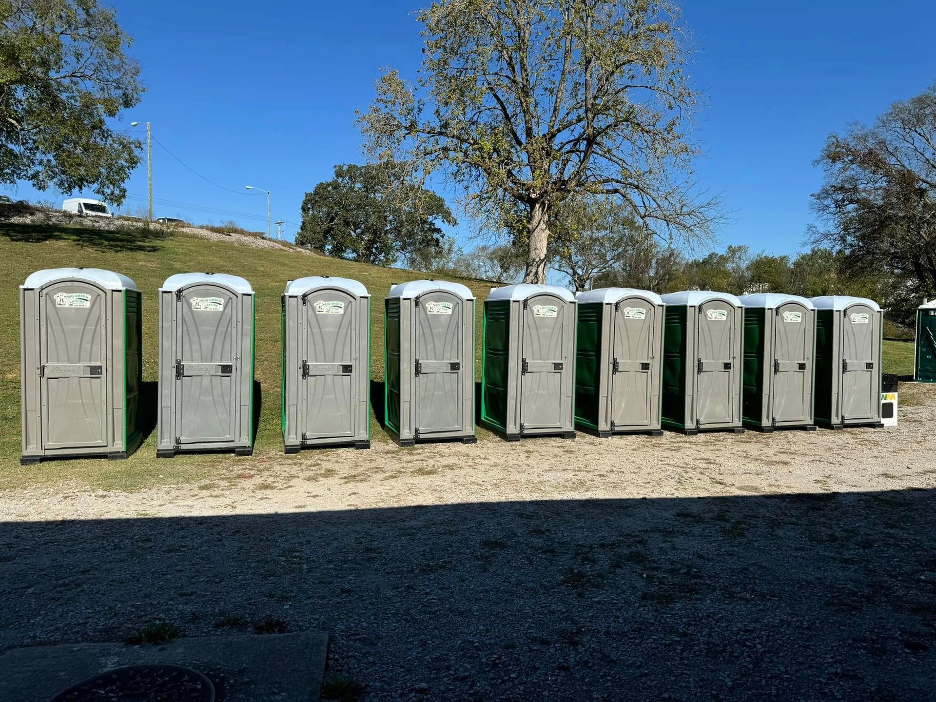 Row of portable toilets on gravel under a blue sky with trees in the background