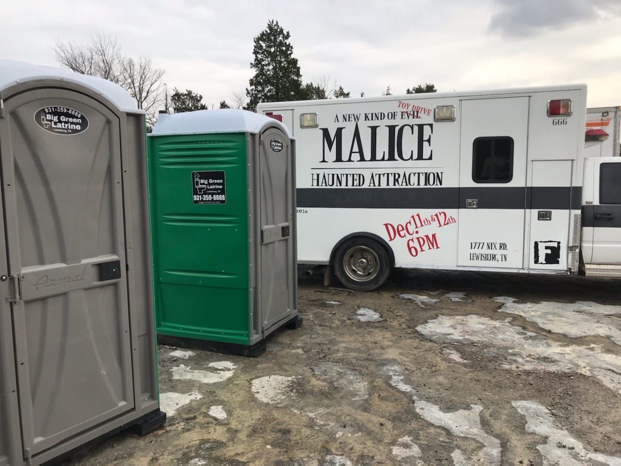 Portable toilets in front of a white “Malice Entertainment” trailer on muddy ground