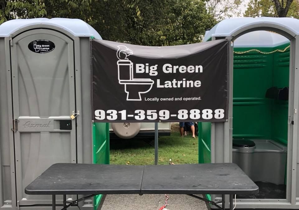 Portable toilets with “Big Green Latrine” banner and phone number at an outdoor event site