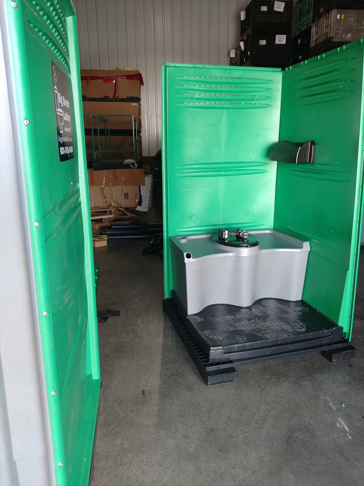 Bright green portable restroom stall with a sink, viewed in a warehouse aisle