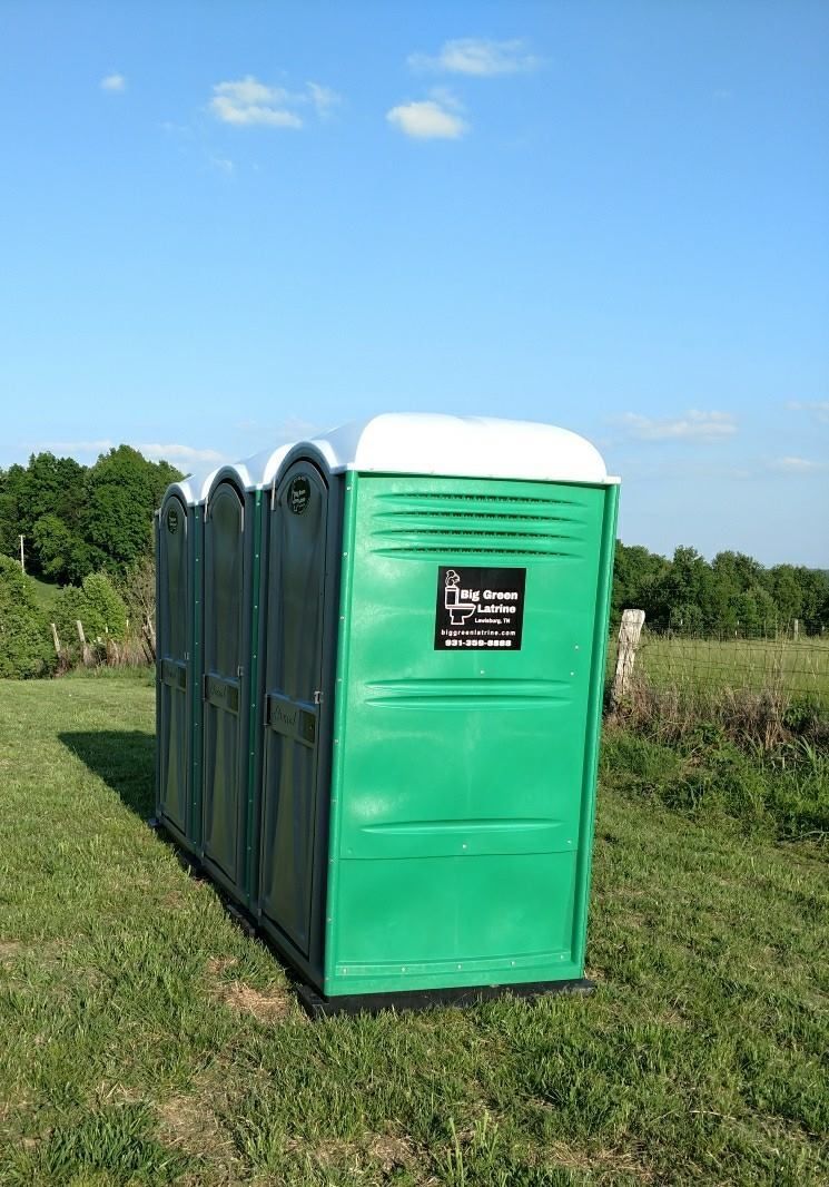 Green portable toilets on a grassy field under a blue sky.