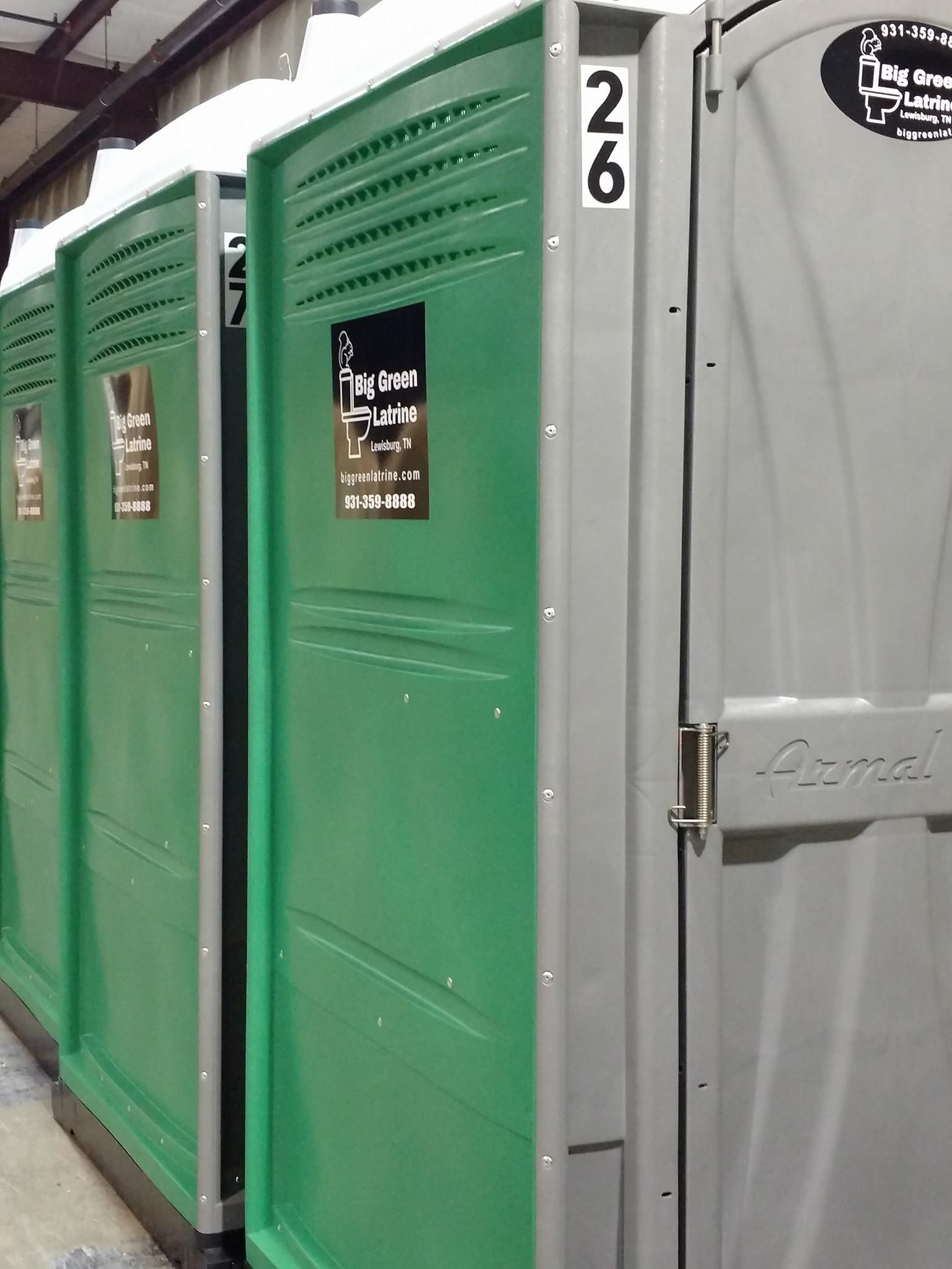 Row of green and gray portable toilets at an outdoor site, numbered 26.