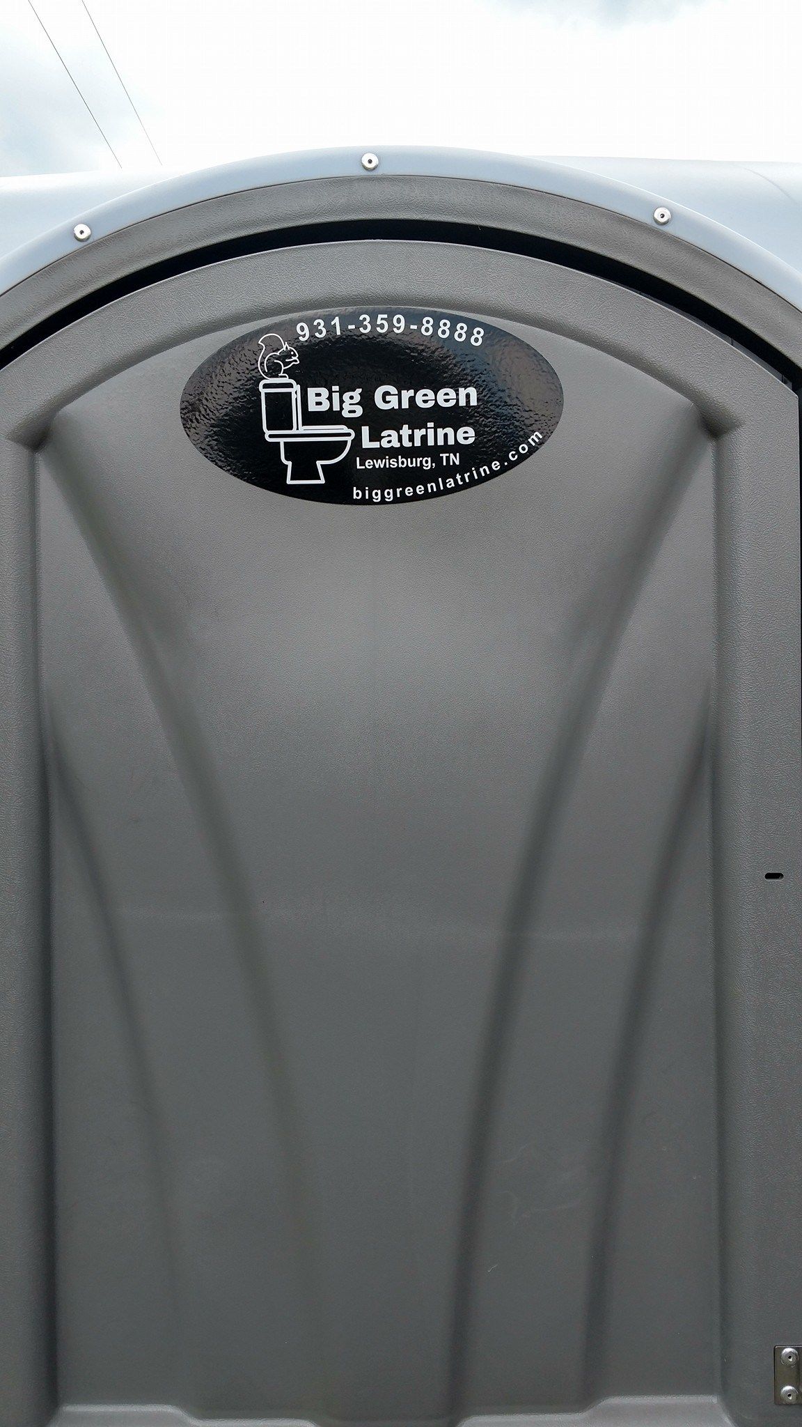 Gray portable toilet with a black “Big Green Loo” sign on the door.
