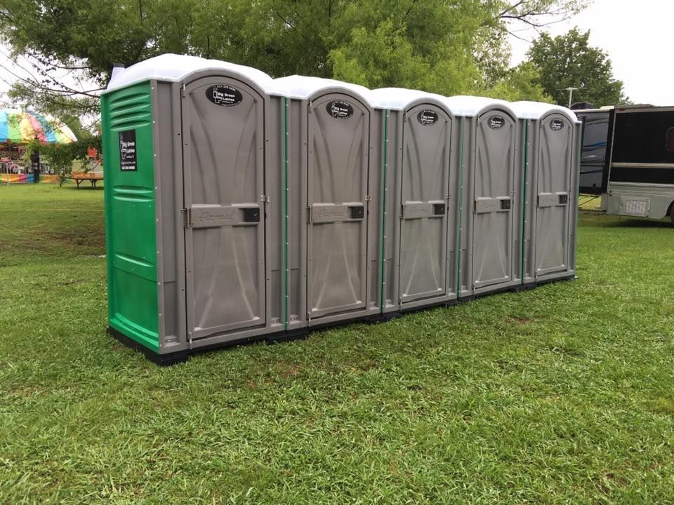 Four gray portable toilets lined up on grass at an outdoor event