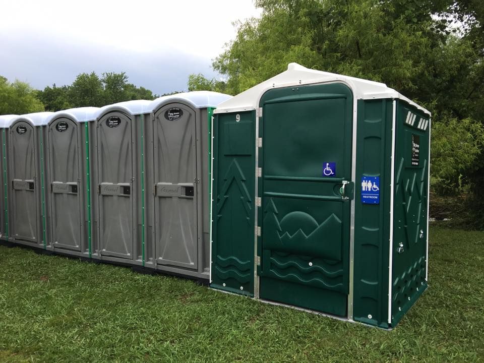 Row of gray and green portable toilets on grass outdoors under cloudy sky