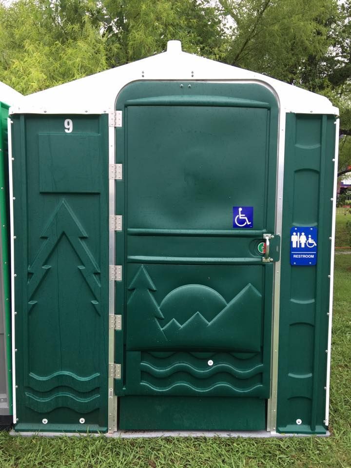 Green portable restroom with accessible door and blue handicap signs outdoors