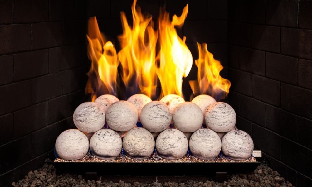 Fireplace with burning flames above ceramic spheres, set against a dark brick background.