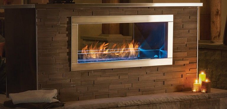 A modern fireplace with flames, framed in silver, set in a stone wall. Candles are lit.