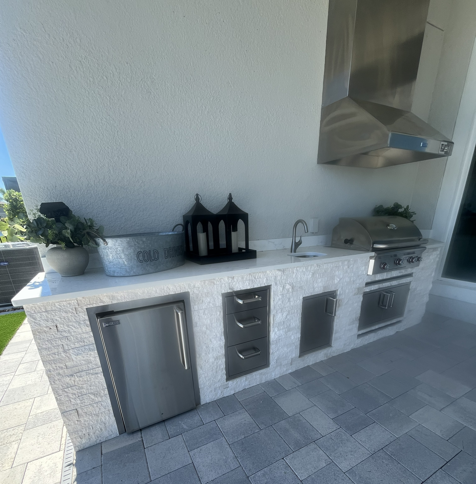 Outdoor kitchen with stainless steel appliances, white countertop, and gray stone facade.