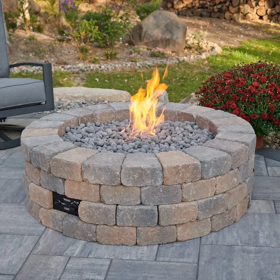 Round brick fire pit with burning flames, gray rocks, and patio setting.