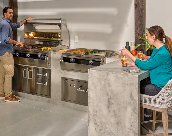 Man grilling food outside, woman seated at a counter. Stainless steel grill and counter with concrete finish.