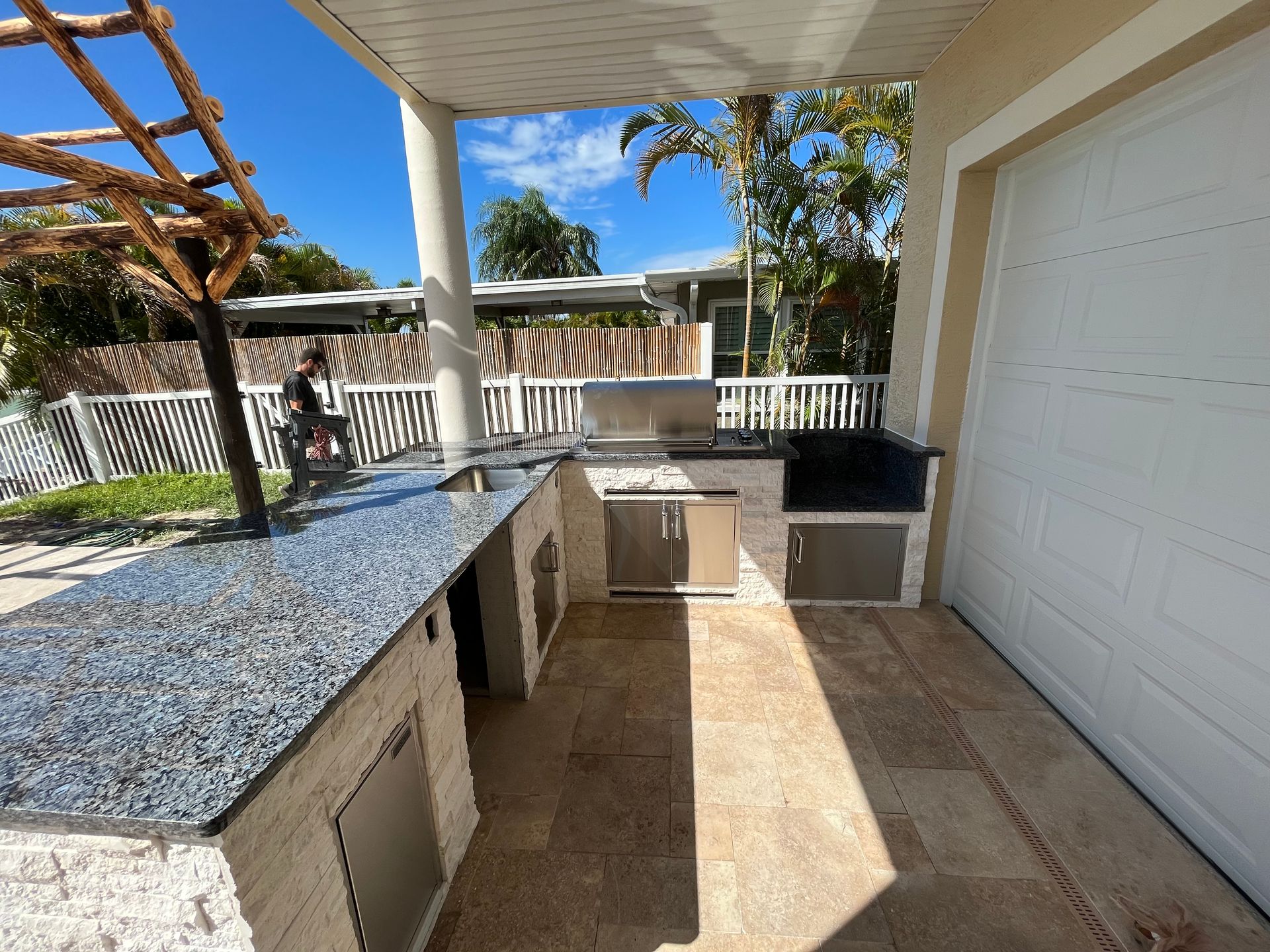 Outdoor kitchen with stainless steel grill, granite countertops, and stone tile flooring.